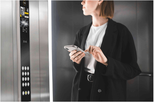 Femme dans un ascenseur tapant sur son téléphone portable l'étage auquel elle se rend.